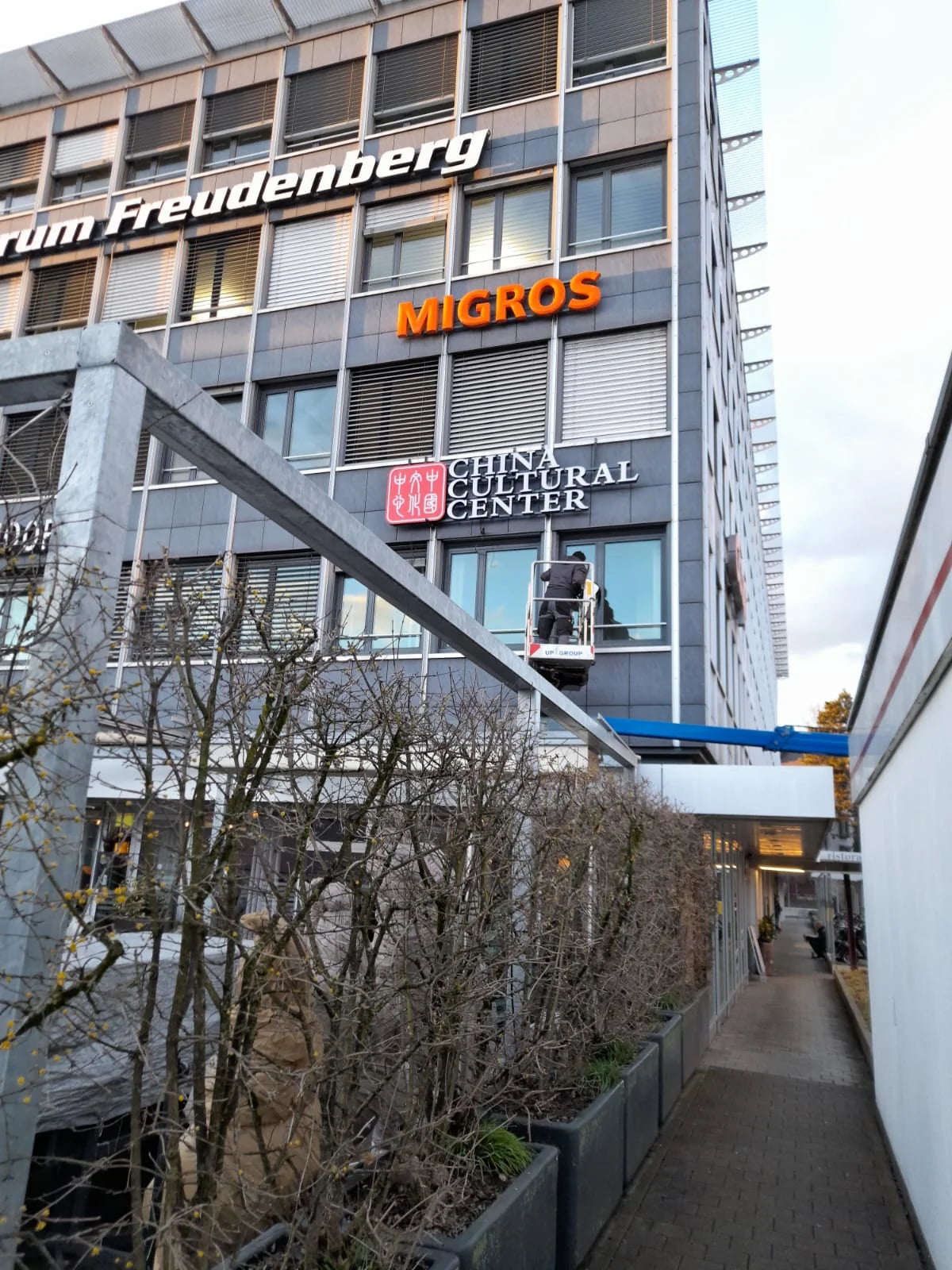 Monteur in einer Hebebühne vor der Leuchtreklame des China Cultural Center an der Fassade des Einkaufszentrums Freudenberg in Bern.