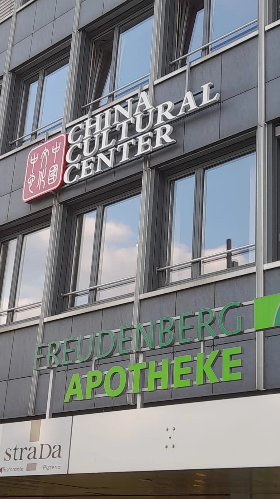 Seitliche Ansicht der dreidimensionalen weissen Buchstaben und des roten Logos des China Cultural Center an der Fassade.