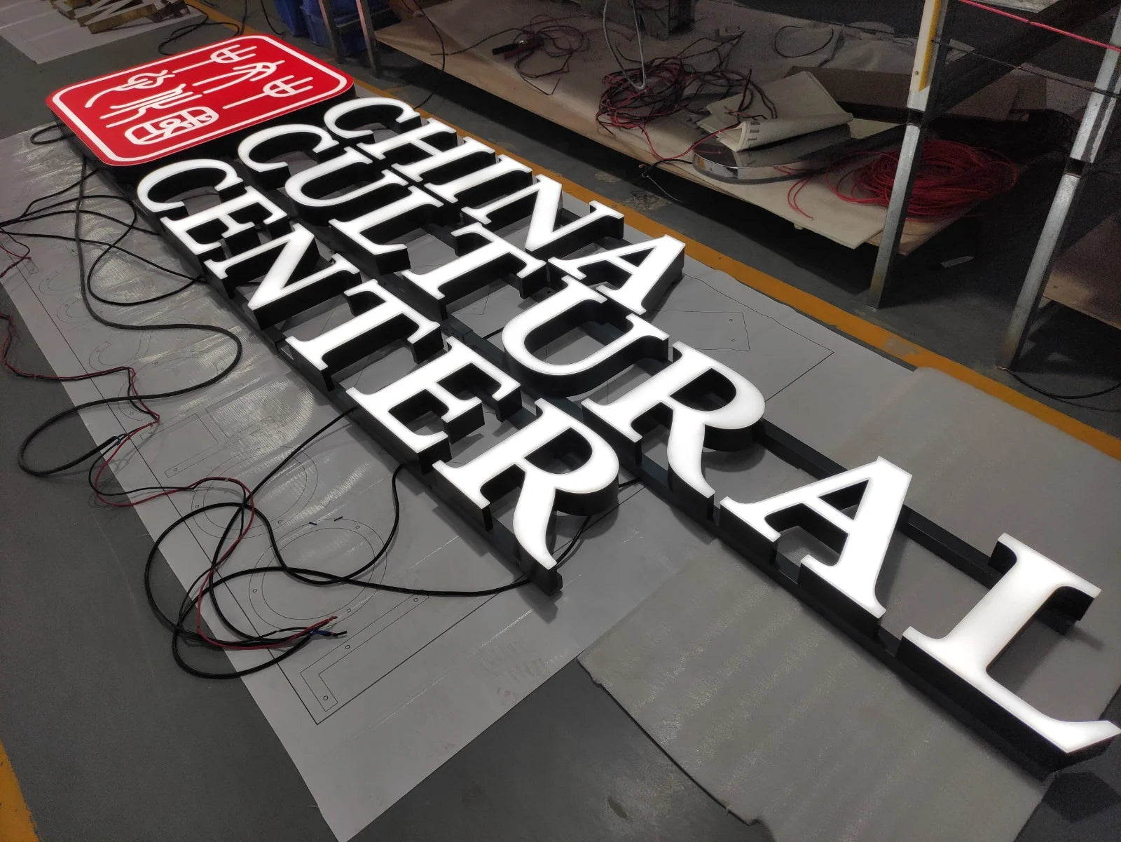 Vollständige Leuchtreklame des China Cultural Center mit rotem Logo und dreidimensionalen weissen Buchstaben, vor der Installation in Bern in der Werkstatt zusammengestellt.