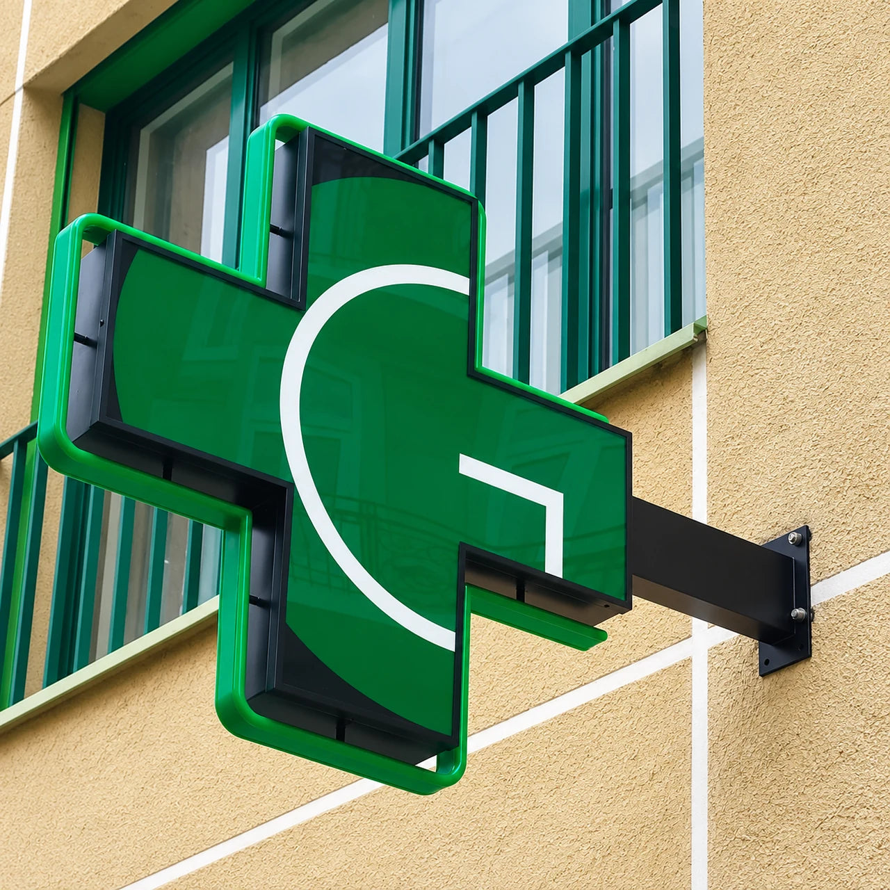 Completed green pharmacy cross with illuminated edging installed on its wall bracket in Clarens, Vaud.
