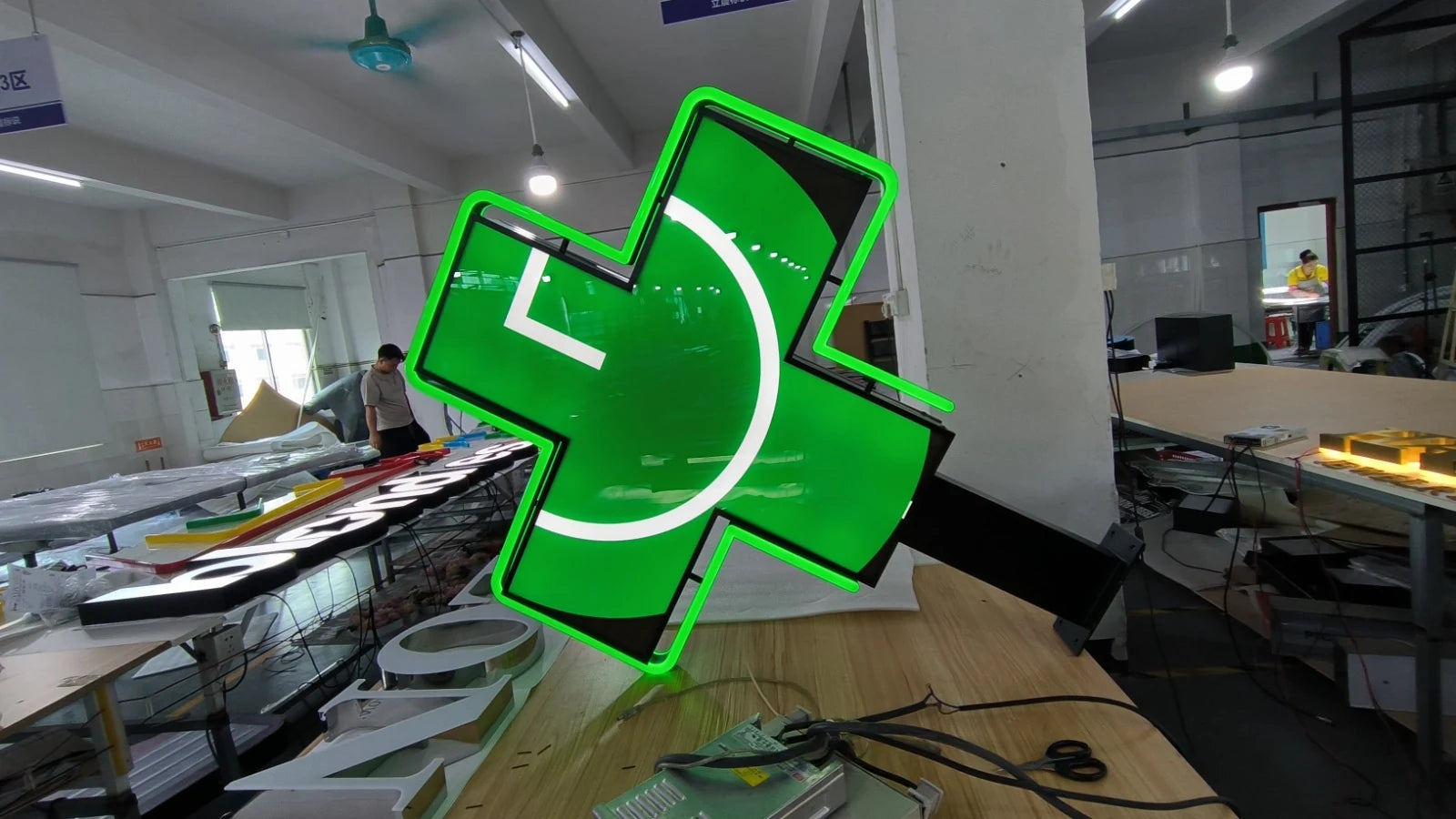 Grüne Seite des Apothekenkreuzes in der Werkstatt mit weissem Motiv und leuchtender grüner Kontur.