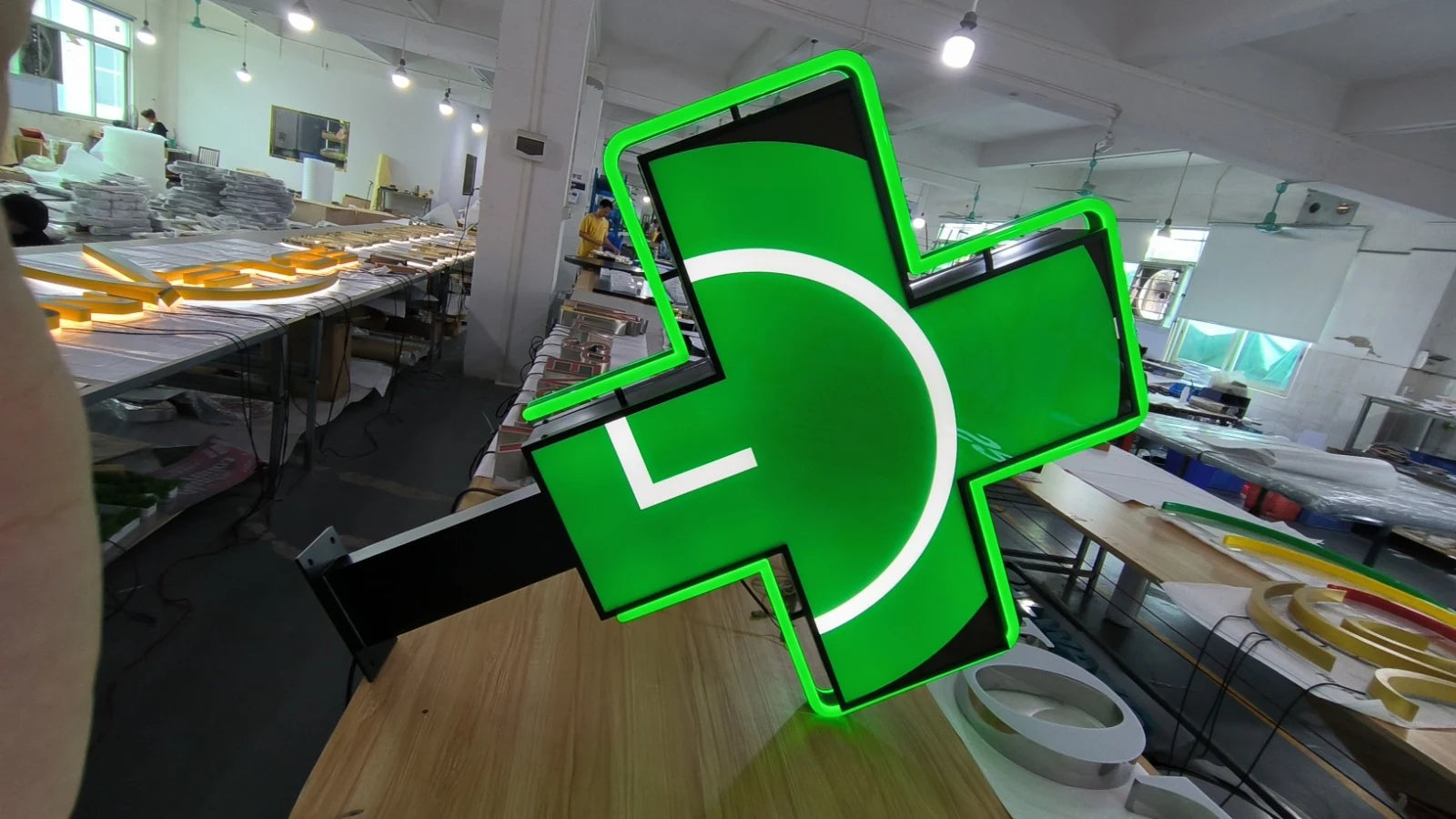 Gegenüberliegende Seite des beleuchteten grünen Apothekenkreuzes in der Werkstatt mit weissem Motiv und schwarzem Ausleger.