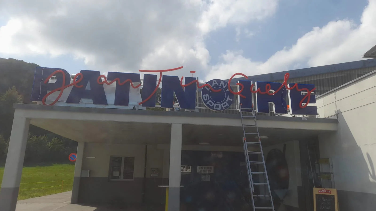 The new sign on the ice rink building in Marly during installation, with a ladder on site.