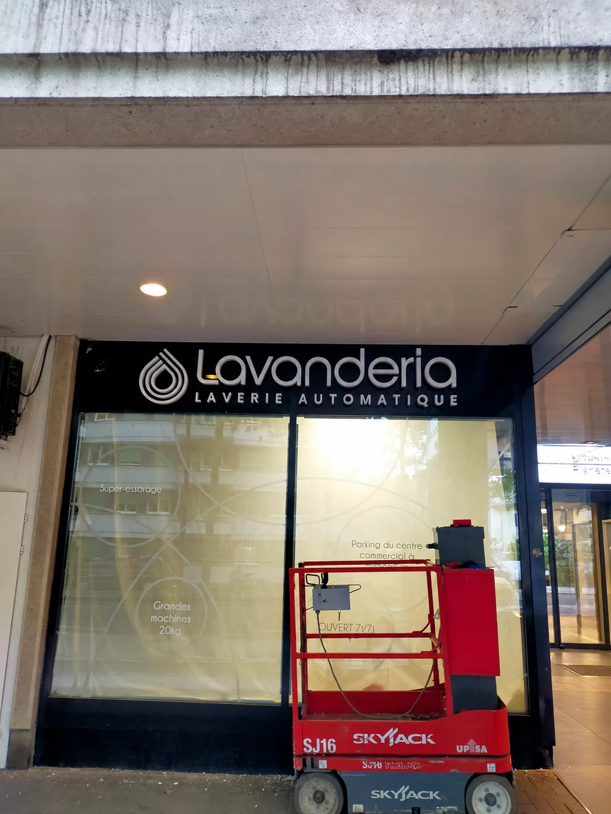 Montage der Lavanderia-Leuchtreklame in Genf mit einer roten Hubplattform vor der Fassade.