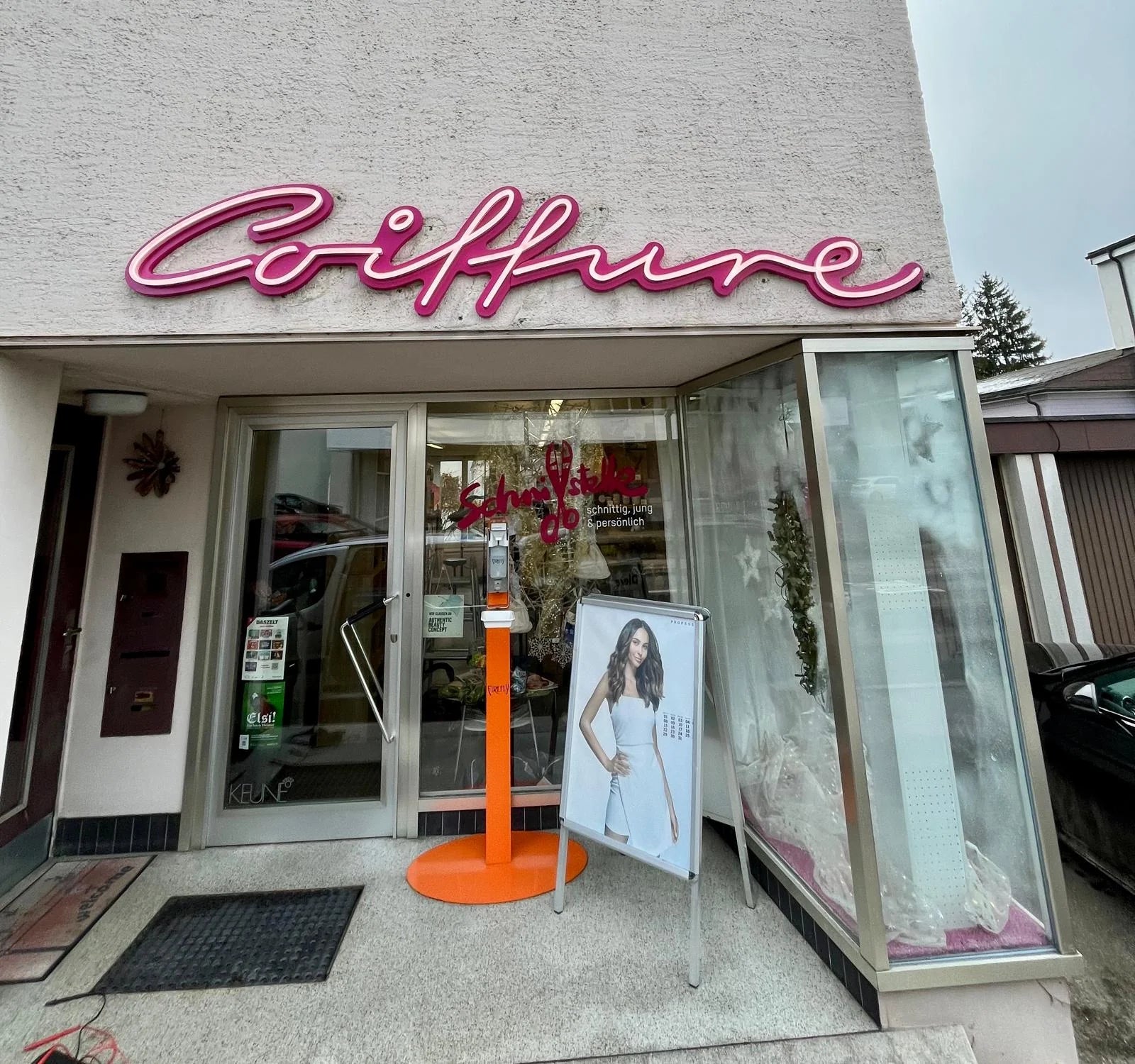 Magentafarbene Coiffure-Leuchtschrift an der hell verputzten Salonfassade in Konolfingen, über dem Eingang und dem Schaufenster.