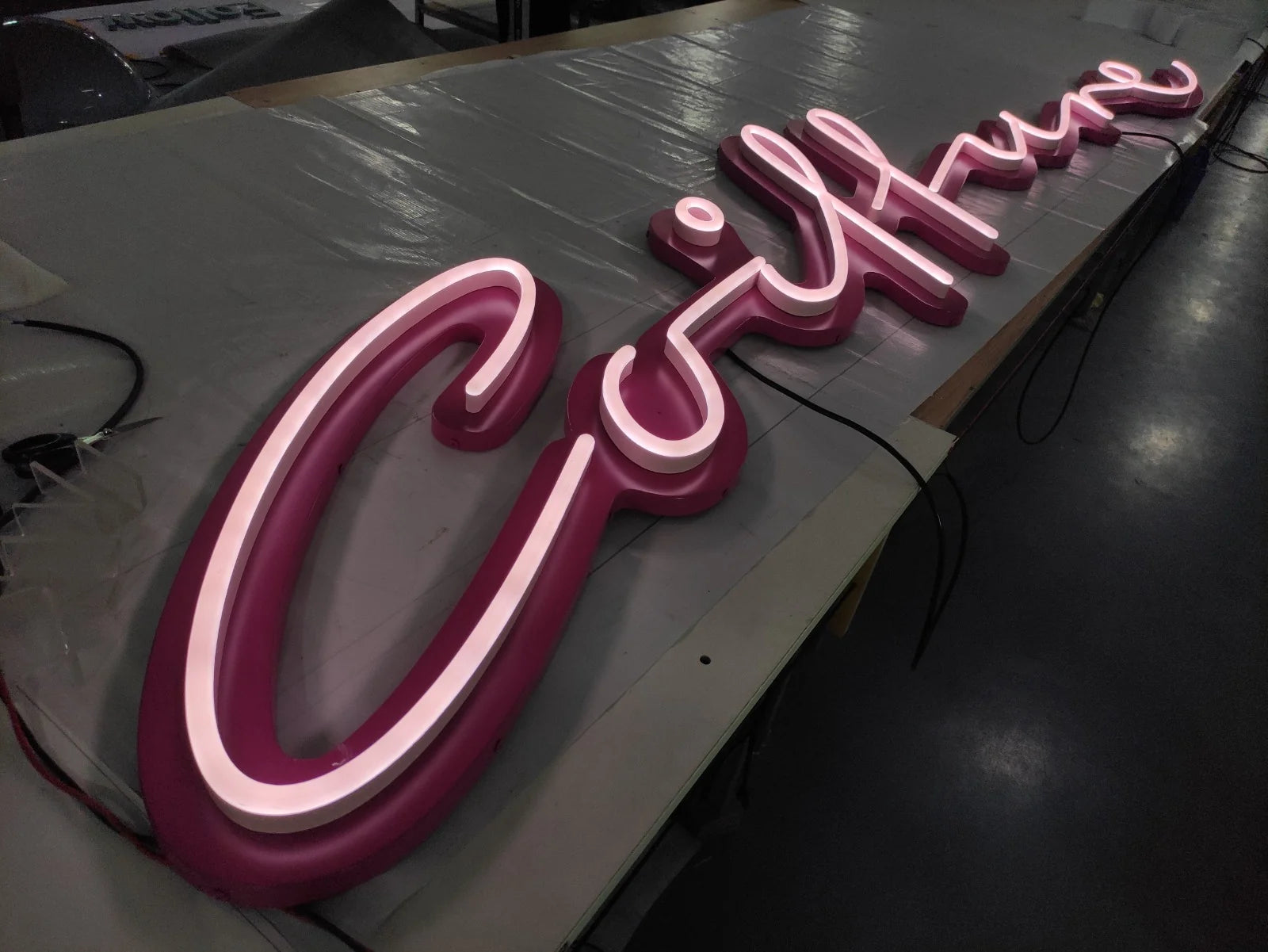 Eingeschaltete Coiffure-Leuchtschrift in der Werkstatt, perspektivisch vom Schwung des C aus gesehen, mit einer Leuchtlinie entlang des gesamten Wortes.