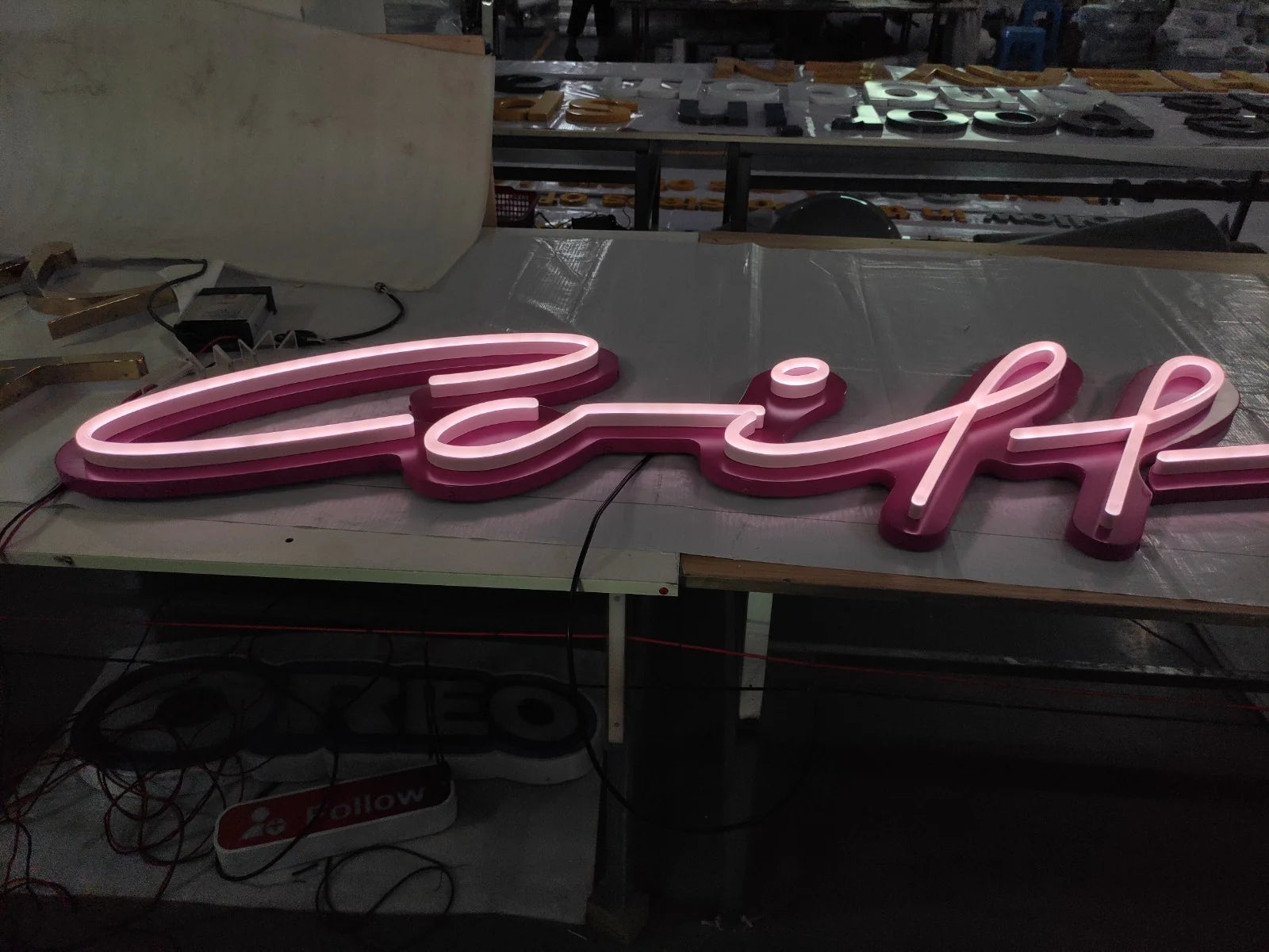 Eingeschaltete Coiffure-Leuchtschrift auf einem Werkstatttisch mit heller Leuchtlinie und magentafarbenem Hintergrund.