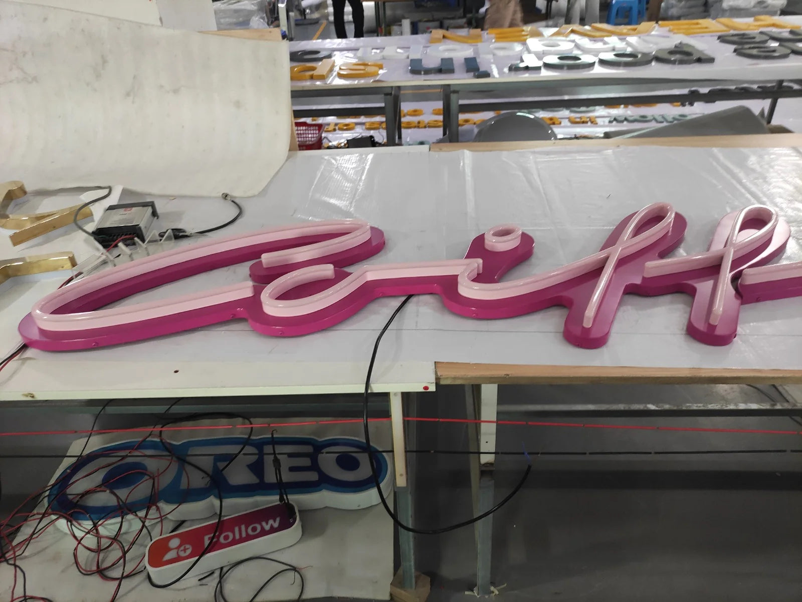 Linker Teil der Coiffure-Leuchtschrift auf einem Werkstatttisch vor dem Einschalten, mit magentafarbenem Hintergrund und heller Linie.