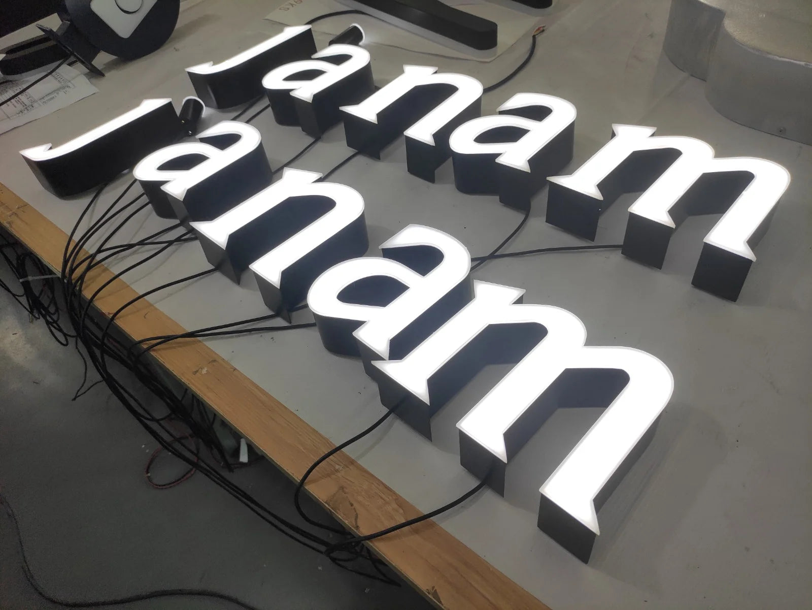 Angled view of the dimensional janam letters on the preparation table, with white illuminated faces and black sides.