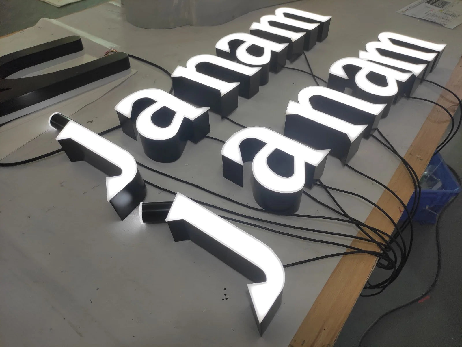 Angled view of the illuminated janam letters in the workshop, showing the depth of the black sides and the white faces.